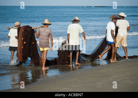 Cinq hommes portant un filet de pêche sur la plage, plage de Morjim, Goa, Inde Banque D'Images