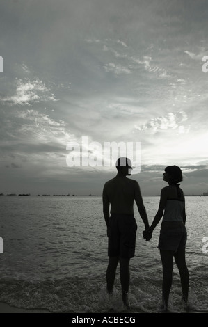 Silhouette d'un couple holding hands and standing on the beach Banque D'Images