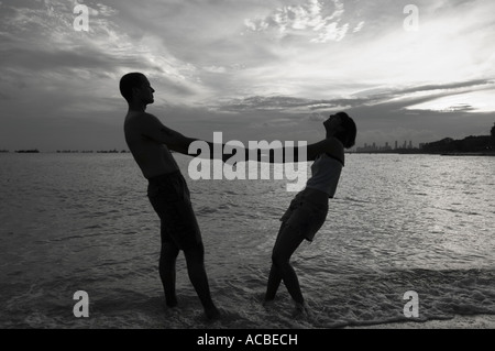 Silhouette d'un couple holding hands and standing on the beach Banque D'Images