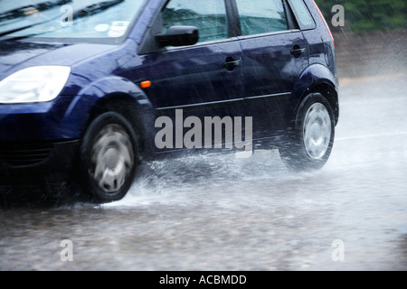 Voiture roulant à travers une route inondée pendant une forte pluie douche Banque D'Images