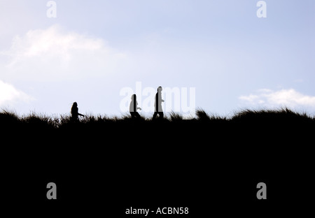 Silhouettes de trois personnes marchant à travers l'ammophile on Sand Dune Ridge Banque D'Images