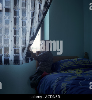 Un jeune garçon regarde par la fenêtre de sa chambre à coucher, salle du Conseil, au Royaume-Uni. Banque D'Images