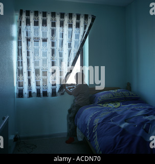 Un jeune garçon regarde par la fenêtre de sa chambre à coucher, salle du Conseil, au Royaume-Uni. Banque D'Images