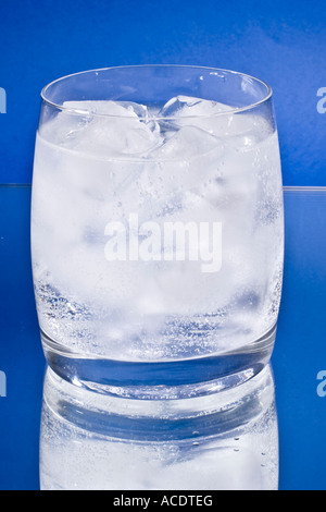 Verre à boire avec de l'eau pétillante et des cubes de glace sur un miroir Banque D'Images