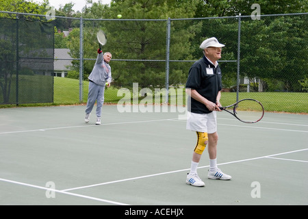 Les hommes retraités âgés jouant un double jeu de tennis dans le cadre d'un tournoi de Jeux olympiques à un établissement de soins continus Banque D'Images