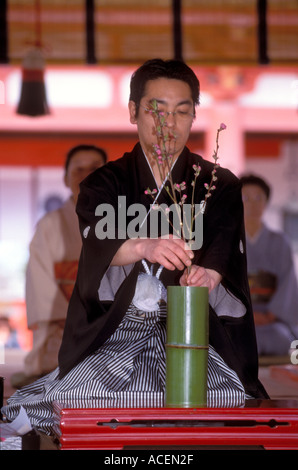 Un homme portant une tenue de kimono traditionnelle dispose des fleurs d'ikebana dans un vase en bambou lors d'une cérémonie à Kyoto, au Japon. Banque D'Images