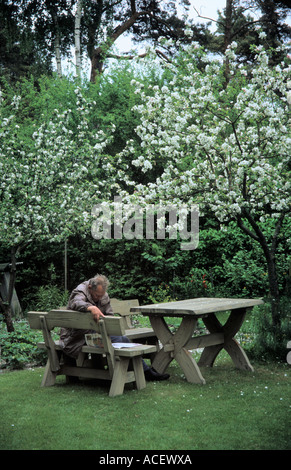 Man reading newspaper sous les pommiers en fleurs dans la ville de Jurmala Lettonie jardin arrière Banque D'Images