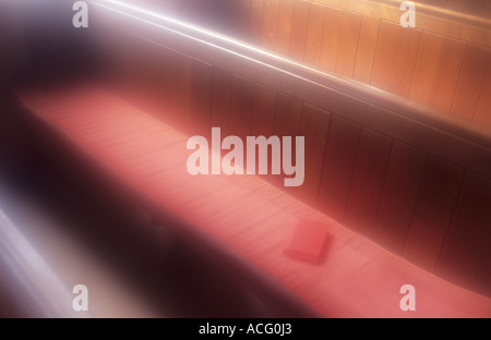 Des bancs d'église en bois simple avec coin rouge baigné de lumière dorée coussins avec siège allongé sur le livre rouge Banque D'Images