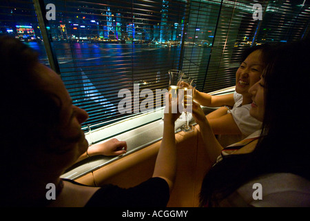 Trois femmes Toasting Chamagne en face de Hong Kong Skyline Felix Bar Peninsula Hotel Kowloon Hong Kong Banque D'Images