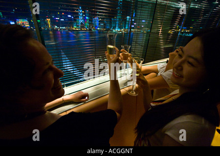 Trois femmes Toasting Chamagne en face de Hong Kong Skyline Felix Bar Peninsula Hotel Kowloon Hong Kong Banque D'Images