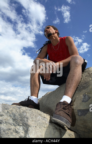 Jeune homme avec des dreadlocks assis sur des rochers Banque D'Images