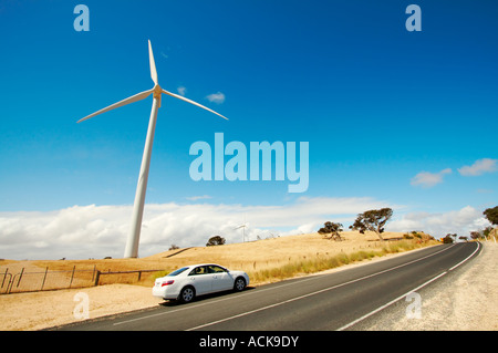 Moulins à vent produisant de l'électricité à une ferme éolienne contre un ciel bleu, à côté de route de campagne. Banque D'Images