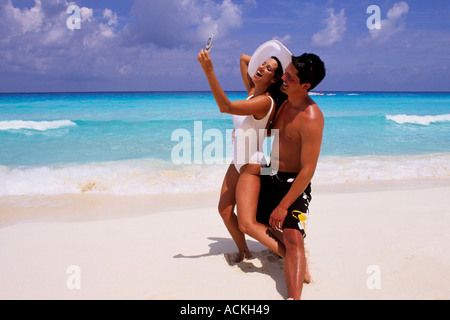 Fun Hispanic couple en utilisant leur téléphone cellulaire sur les plages de Cancun au Mexique Banque D'Images