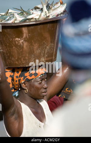 Les jeunes femmes portent des bassins de poissons frais sur la tête de plage sur le marché aussi ouvrir les bateaux de pêche arrivent avec la Gambie Tanji capture Banque D'Images