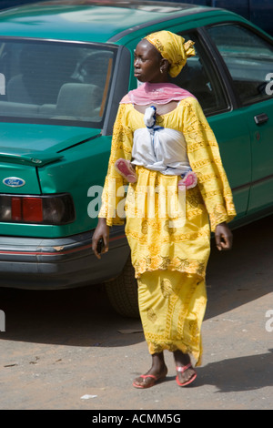 Pieds de bébé en écharpe sous les armes de la femme marche en jaune vêtements traditionnels Bakau Gambie Le Marché Banque D'Images