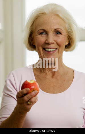 Senior woman eating apple, smiling, portrait, close-up Banque D'Images