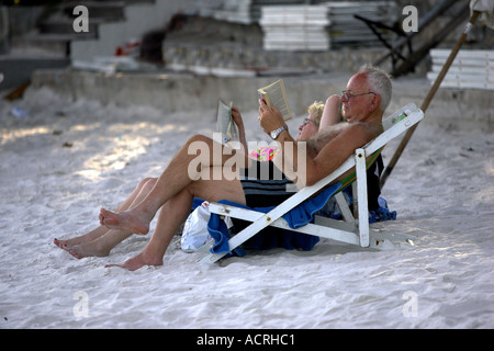 Vieux couple vous détendre dans les chaises longues à lire des livres sur la plage Thaïlande Ko Samet Banque D'Images