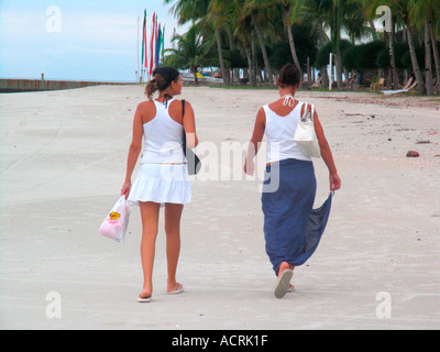Deux jeunes femmes à pied sur la plage de Pantai Cenang Malaisie Pulau Langkawi island Banque D'Images