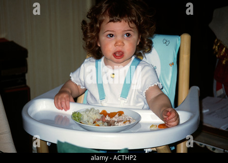 Dix-huit mois du Girl eating dans une chaise haute Banque D'Images