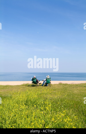 Un couple de personnes âgées assis sur des chaises pliantes et profitant d'un après-midi ensoleillé sur l'herbe au-dessus de la plage de Slapton. Devon. ROYAUME-UNI Banque D'Images