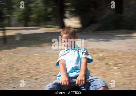 Un garçon de 5 ans sur merry go round dans park blurred motion Banque D'Images