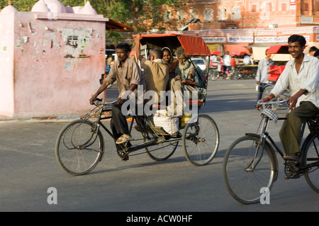 Plusieurs personnes allongées sur un cycle rickshaw et un homme à vélo dans une rue typique scène dans Jaipur. Banque D'Images