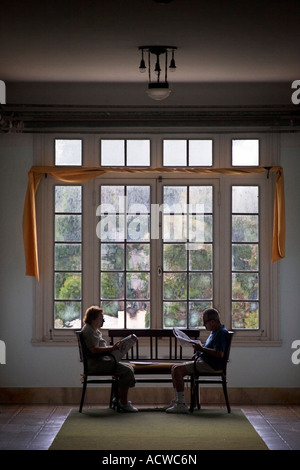 Un vieux couple reading par une fenêtre de hauteur Banque D'Images