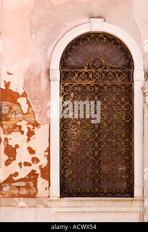 Verticale de l'image couleur d'une porte couverte d'une grille en fer rouillé dans un bâtiment en brique recouverts de stuc rose à Venise Italie Banque D'Images