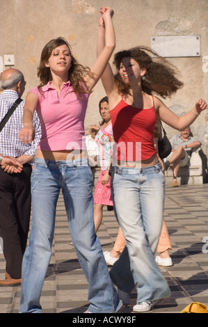 Editorial N'utilisez que le modèle ne libération teenage girls dancing en avril 9 Plaza à Taormina avec bibliothèque municipale et les touristes derrière Banque D'Images