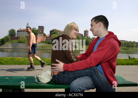 Jeune couple assis sur un banc, dans l'arrière-plan le château de Wawel, à Cracovie, Pologne Banque D'Images