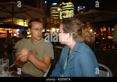 Couple sérieux au bar en plein air dans la nuit avec les lumières de la ville en arrière-plan Banque D'Images