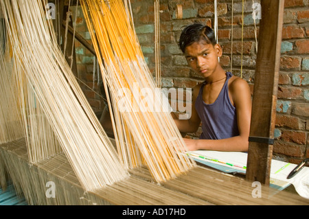 Portrait d'un mince horizontale jeune garçon travaillant dans un métier à tisser des saris en soie dans les usines de backstreet de l'Inde. Banque D'Images