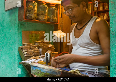 Portrait horizontal d'un propriétaire de magasin indien rouler des cigarettes en vente à sa boutique vers le bas une ruelle à Varanasi. Banque D'Images