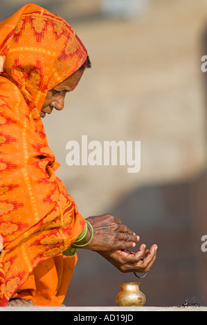 Une vieille femme indienne portant un châle de couleur orange dans la prière à un Ghat de Varanasi. Banque D'Images