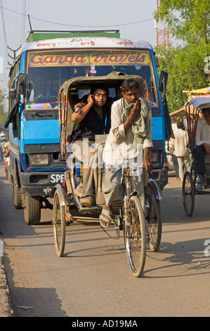 Un scènederue chaotique typique à Varanasi - un cycle rickshaw et passager sur un téléphone mobile avec un Ganga Voyages voiture derrière. Banque D'Images