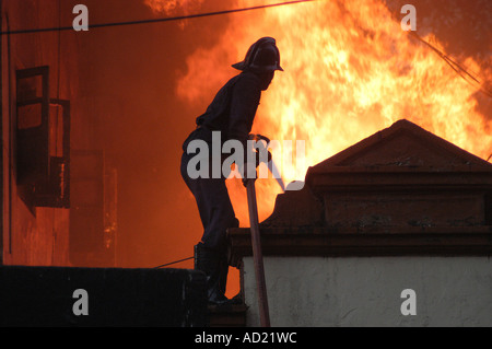 Pompier sur le dessus de toit de maison en feu feu rouge lutte contre les flammes avec de l'eau tuyau d'incendie Banque D'Images