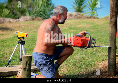 Un homme utilise une scie et niveau laser comme il coupe des capacités des souches ou des supports pour deck autour de sa maison Banque D'Images