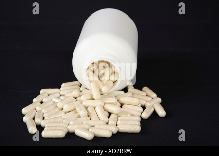 Bouteille ordinaire blanc transparent rempli de capsules débordent de couleur beige fond. Banque D'Images