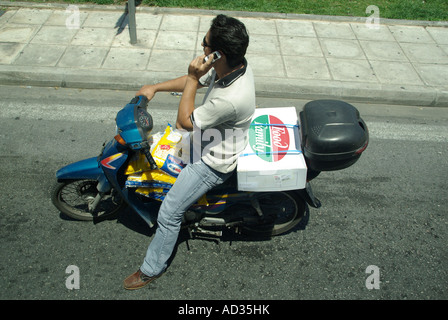 Homme d'Athènes en scooter l'attente aux feux de circulation chatting on mobile phone bike chargé de sacs de croustilles Banque D'Images