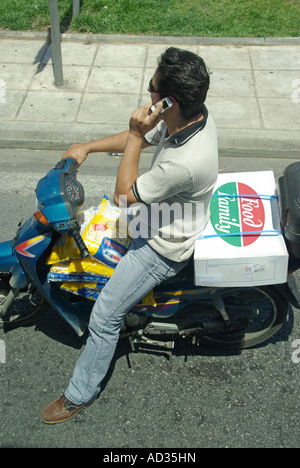 Athènes vue franche d'un homme en scooter qui attend aux feux de signalisation discutant sur un téléphone portable vélo chargé de sacs de jetons Grèce Banque D'Images