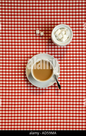 Tasse et soucoupe thé blanc sur rouge et blanc en tissu à carreaux au-dessus de la table avec un bol de cubes de sucre Banque D'Images