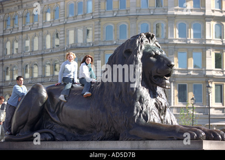 Les touristes s'asseoir sur le dos d'une statue de lion à Trafalgar Square, Londres, Angleterre, Royaume-Uni Banque D'Images