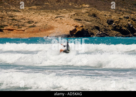 Vue horizontale d'un homme de race blanche kitesurfer dans une position accroupie s'écraser à travers les vagues dans le soleil Banque D'Images