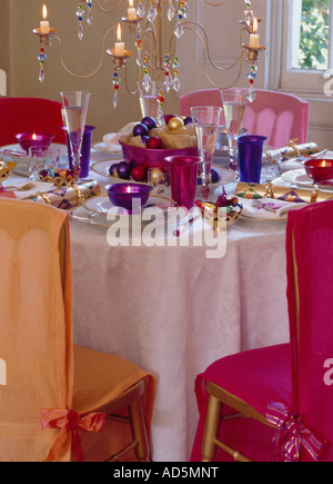 Rose et orange loosecovers sur des chaises à Noël avec table en verre violet bougeoirs et candélabres en verre tableau ci-dessus Banque D'Images