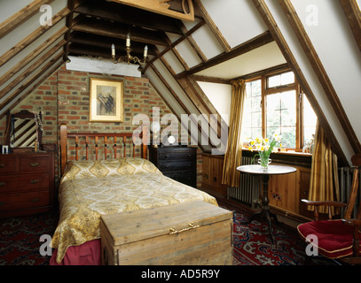 Coffre en bois en dessous de lit dans une chambre mansardée avec mur de briques et de poutres apparentes au plafond dans converti moulin Banque D'Images