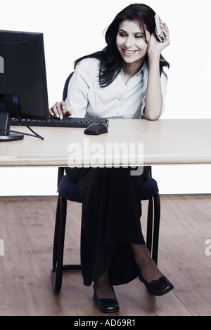 Businesswoman sitting in front of a computer holding a mobile phone Banque D'Images