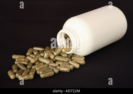 Bouteille en plastique blanc sur le côté à un angle de 45 degrés déversant capsules transparent rempli de pâte vert herbe in pool Banque D'Images