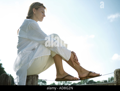 Femme assise sur le dessus de la clôture, low angle view Banque D'Images