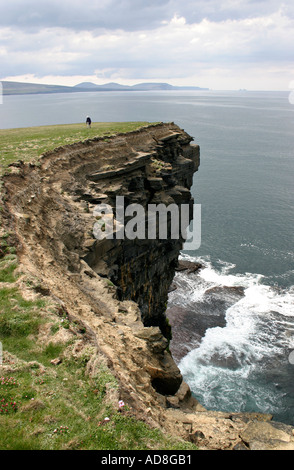 Une femme marche seule dans le soleil sur Downpatrick Head White breakers de la mer briser ci-dessous Banque D'Images