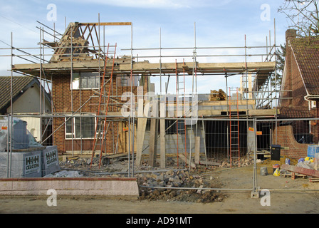 Site de construction maison individuelle en partie démoli pour le remaniement et l'échafaudage érigé pour conversion nouveau toit pile de matériaux England UK Banque D'Images